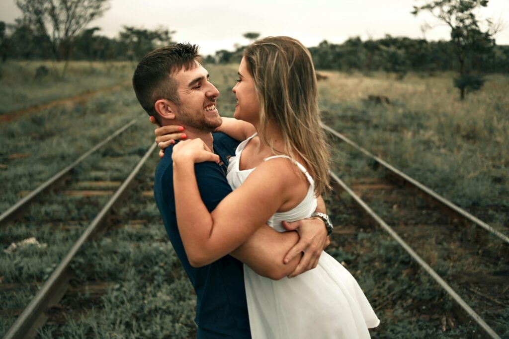 A couple sharing a romantic moment outdoors on railroad tracks in summer.