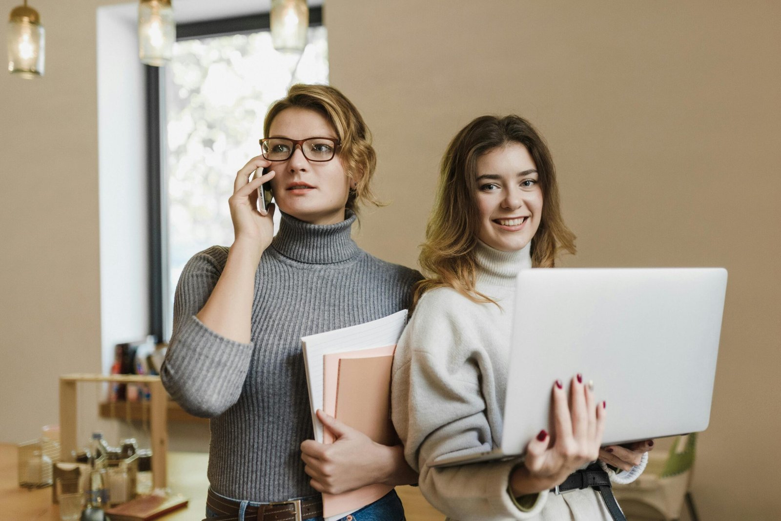 Two women collaborate in a modern office environment, balancing work with technology.