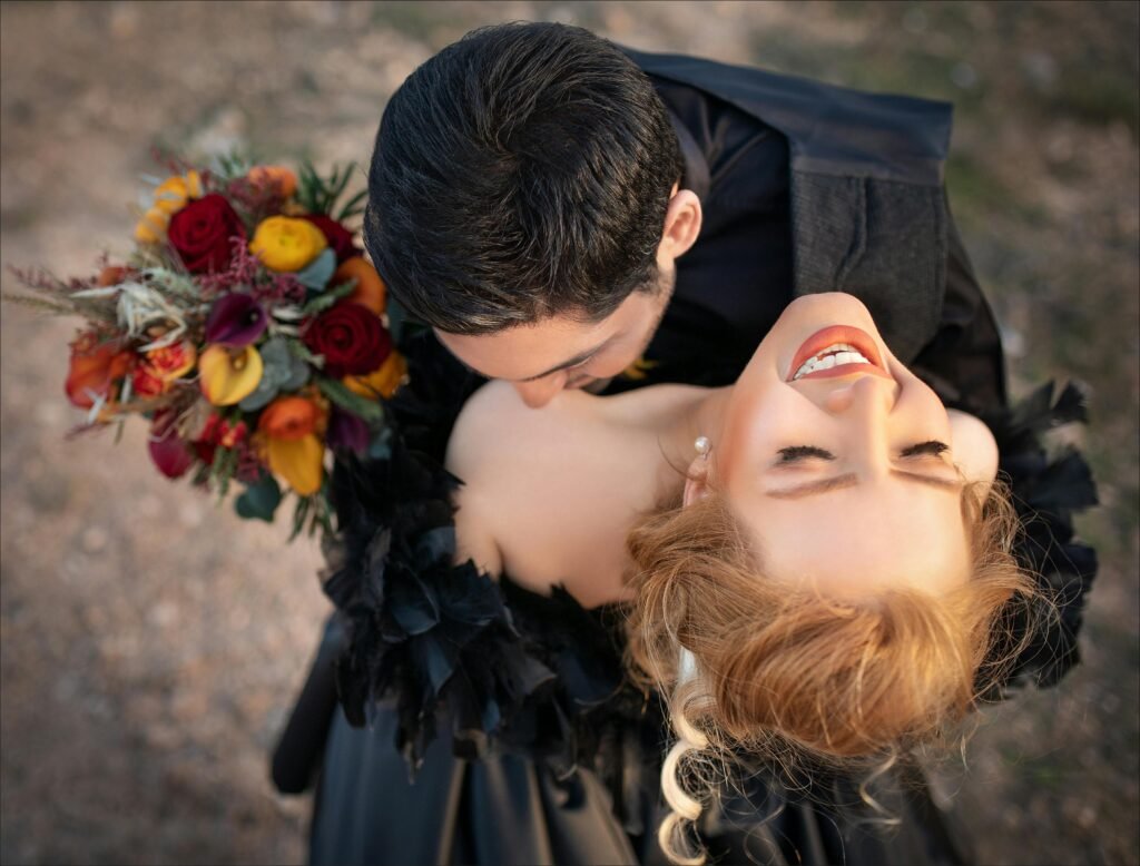 A joyous couple embracing outdoors, holding a vibrant flower bouquet.